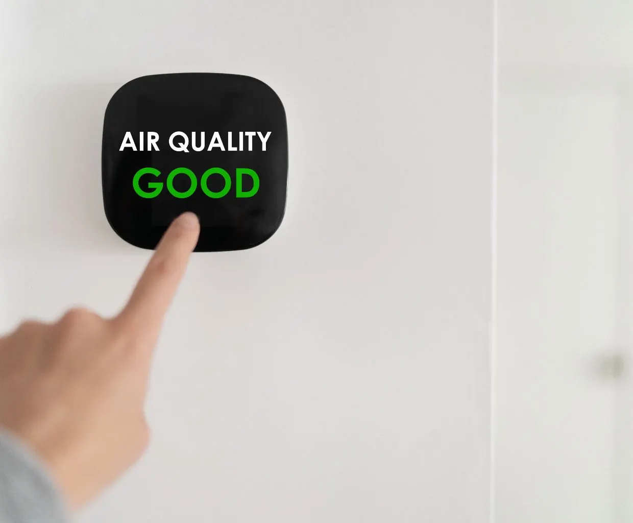 Finger touching a wall-mounted air quality display that reads Air Quality Good