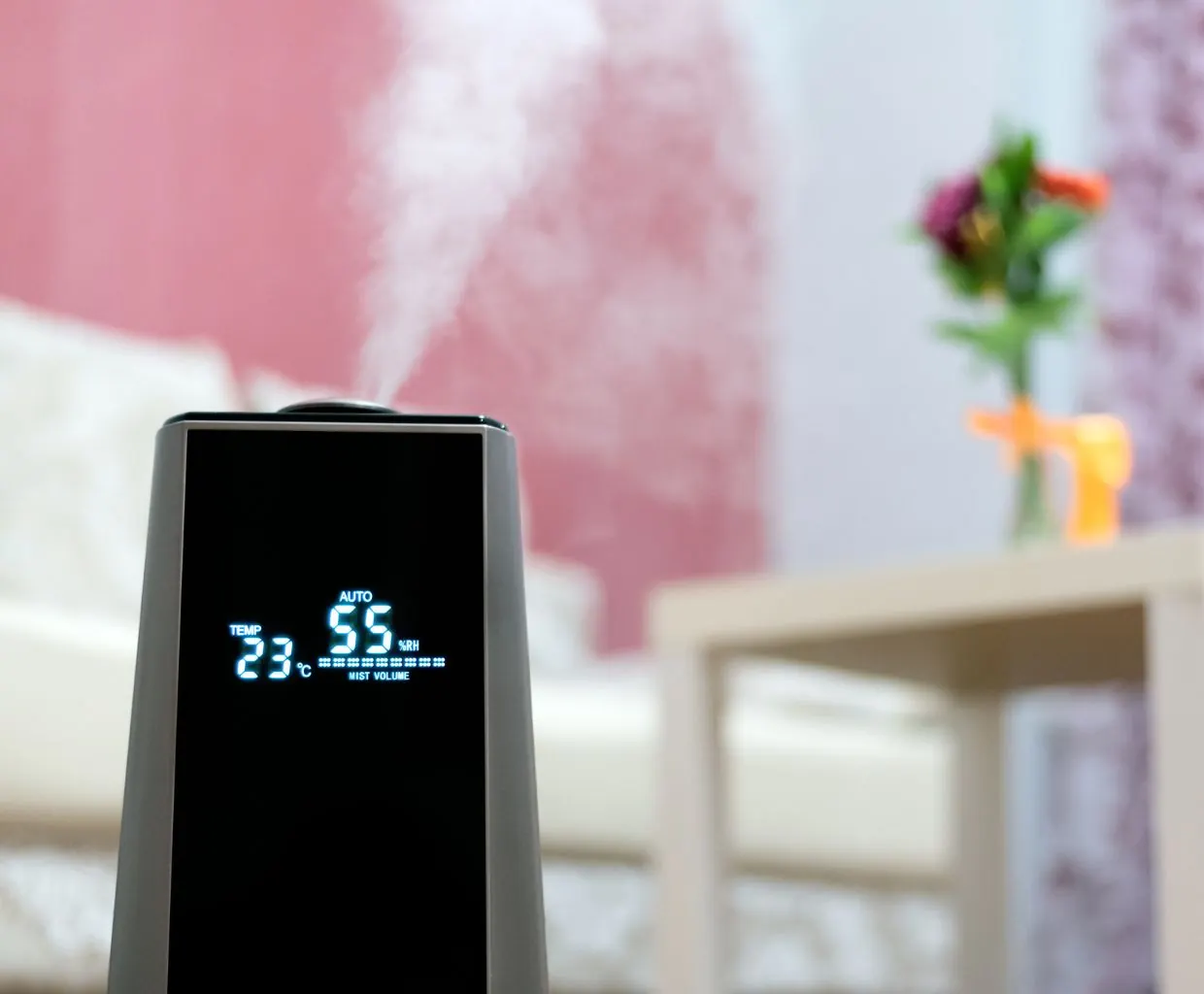 Close-up of a humidifier display reading 23 °C and 55% RH in Auto mode, with mist rising in a living room