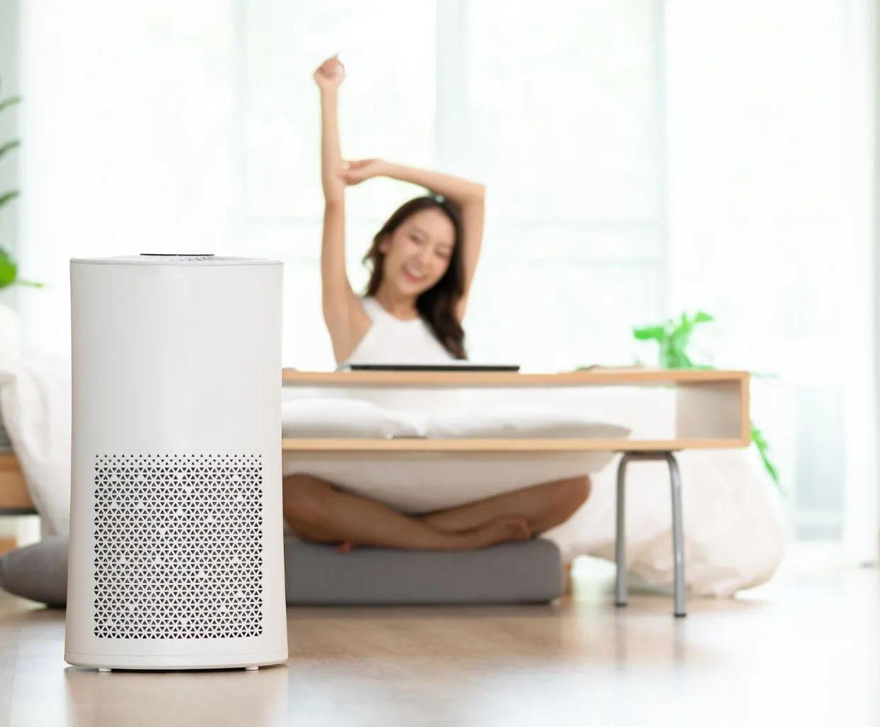 Woman stretching at a low table in a bright room with a white air purifier on the floor