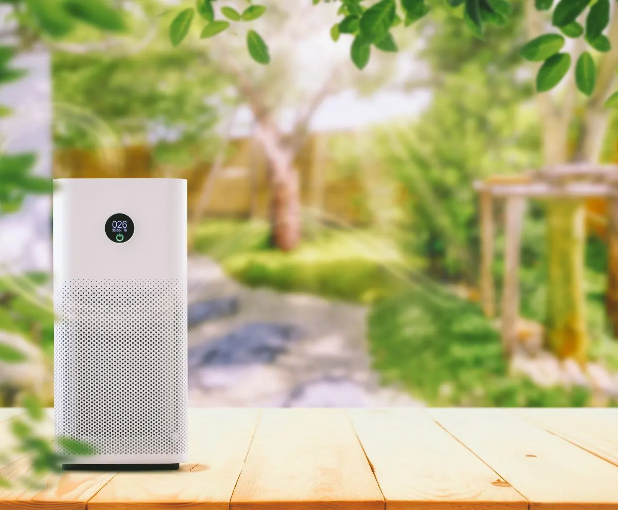 White air purifier with a round digital display on a wooden table in front of a blurred green garden