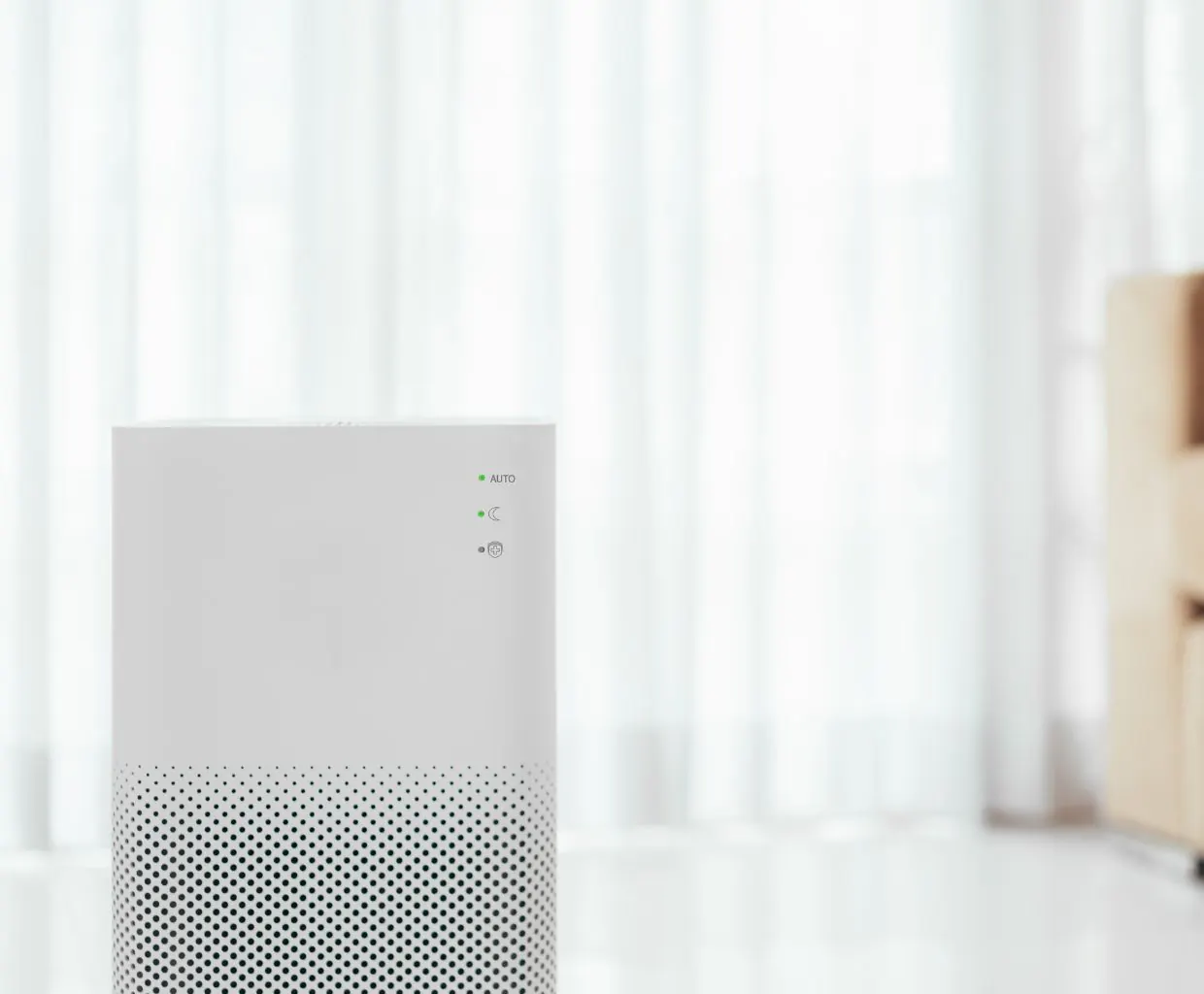 White air purifier standing in a bright room in front of sheer curtains