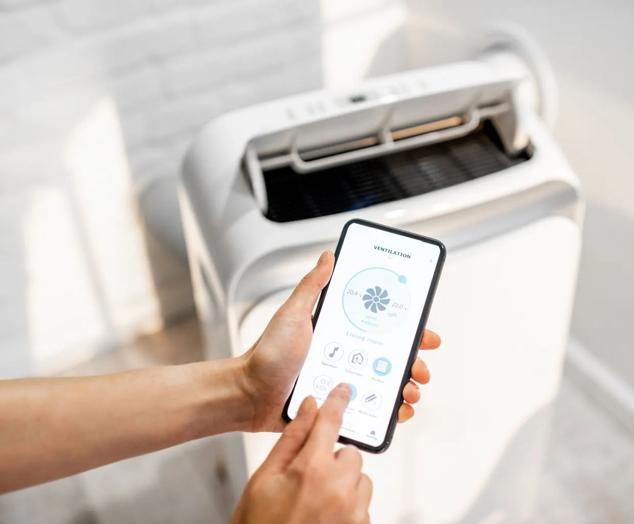 Hand holding a smartphone app in front of a white combination air purifier and humidifier