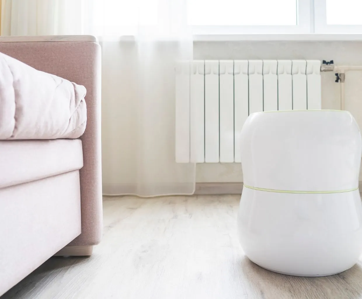 White rounded floor unit beside a pink sofa bed, with a white radiator under a bright window with sheer curtains
