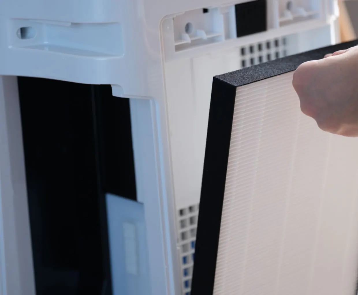 Hand sliding a white pleated HEPA filter with a black foam frame out of an opened white air purifier
