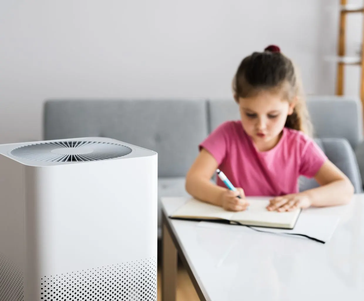 Girl writing in a notebook at a white table, with a white air purifier in the foreground