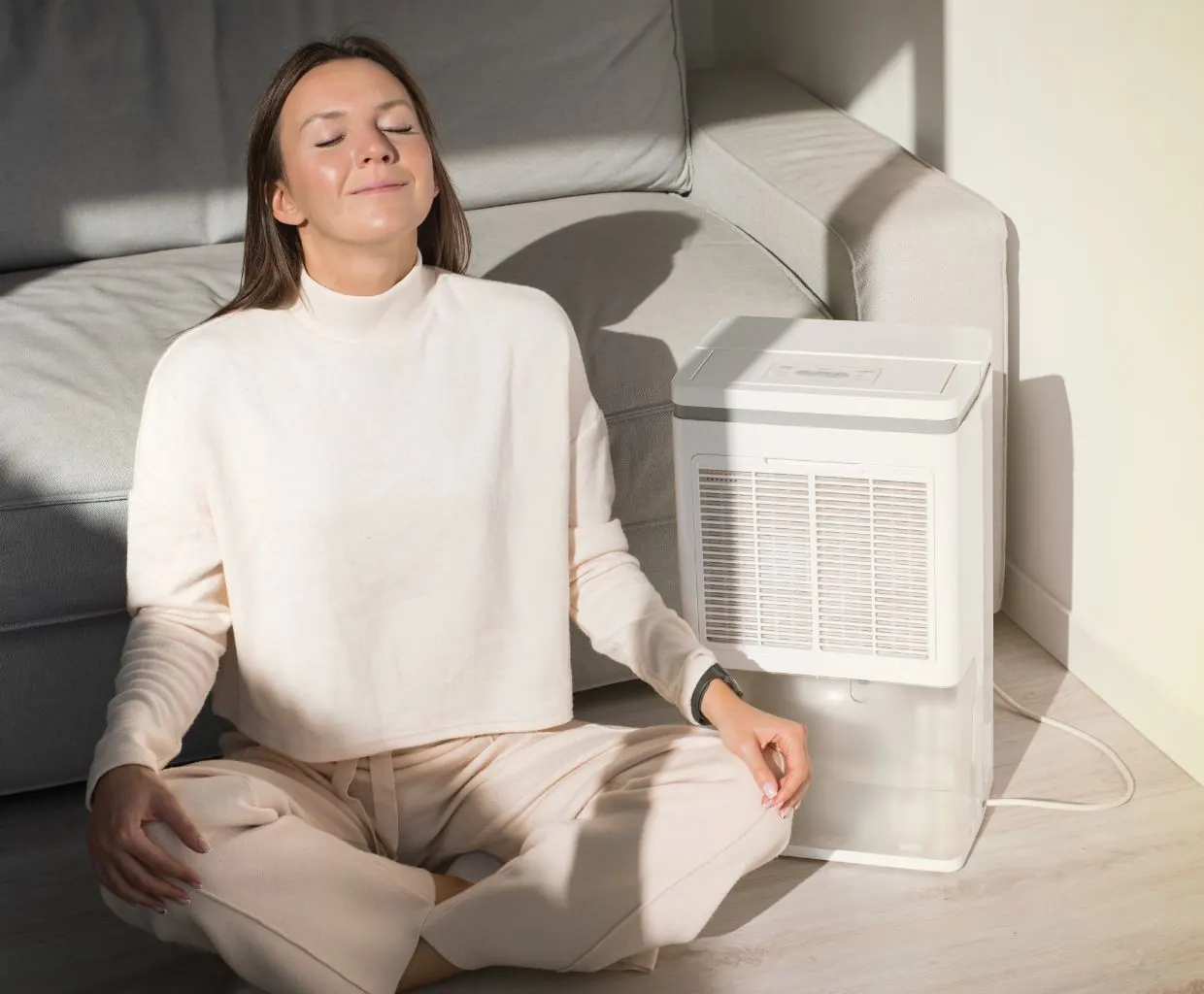 Woman meditating on the floor next to a compact white air purifier