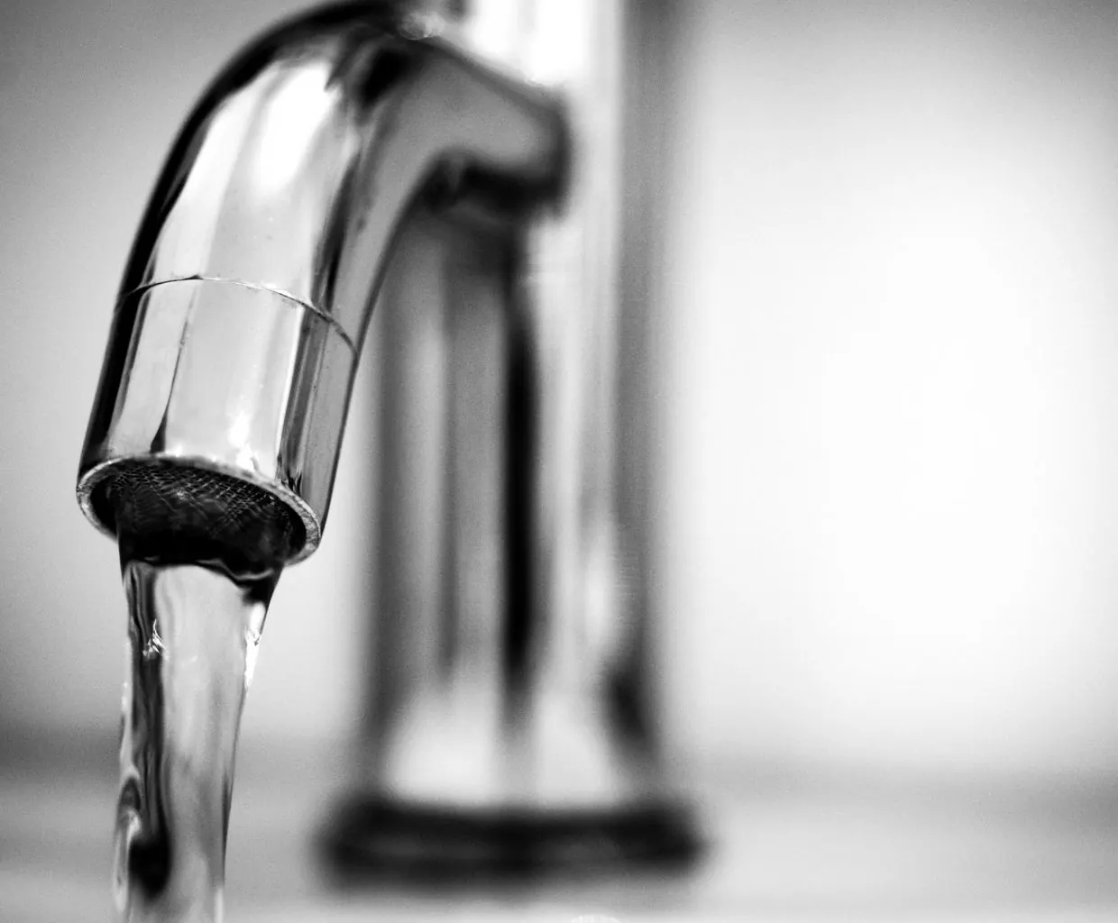 Black and white close-up of tap water running from a chrome kitchen faucet